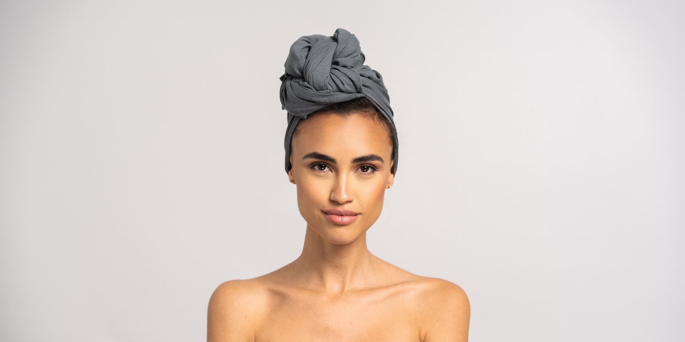 Eine junge hübsche Frau mit dunklen Haaren trägt ein graue Bambus Handtuch von Curly'N'Covered als Turban gewickelt