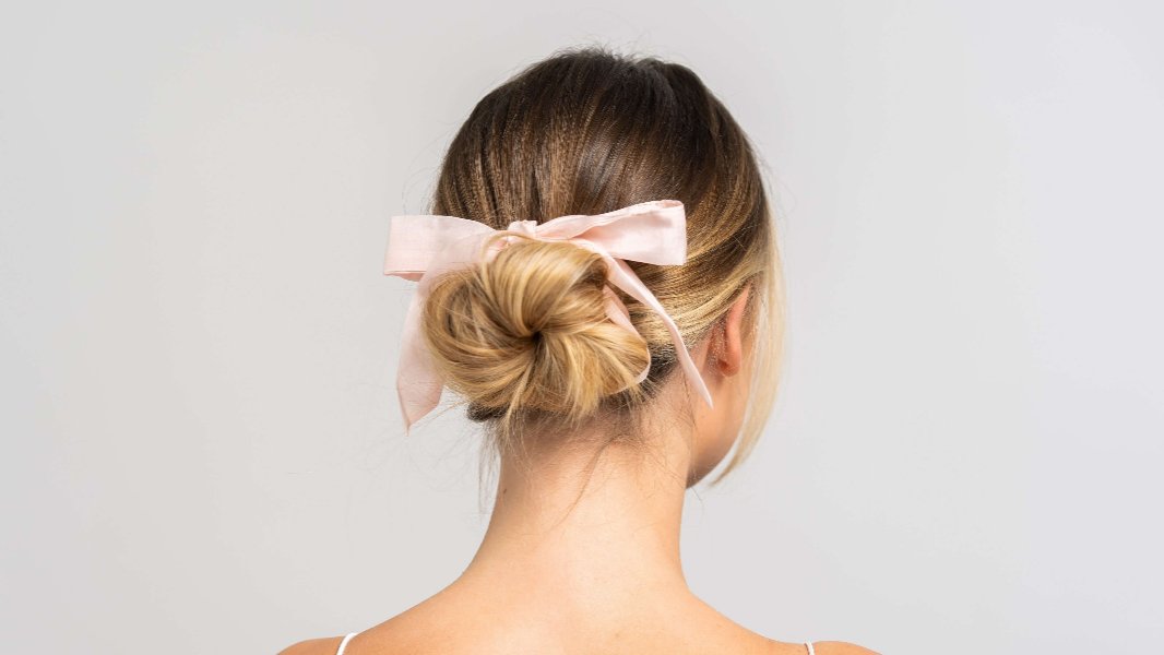 Wunderschöne Frau mit blonden Haaren trägt einen rosa Seidenschal von Curly N Covered als Schleife im Haar