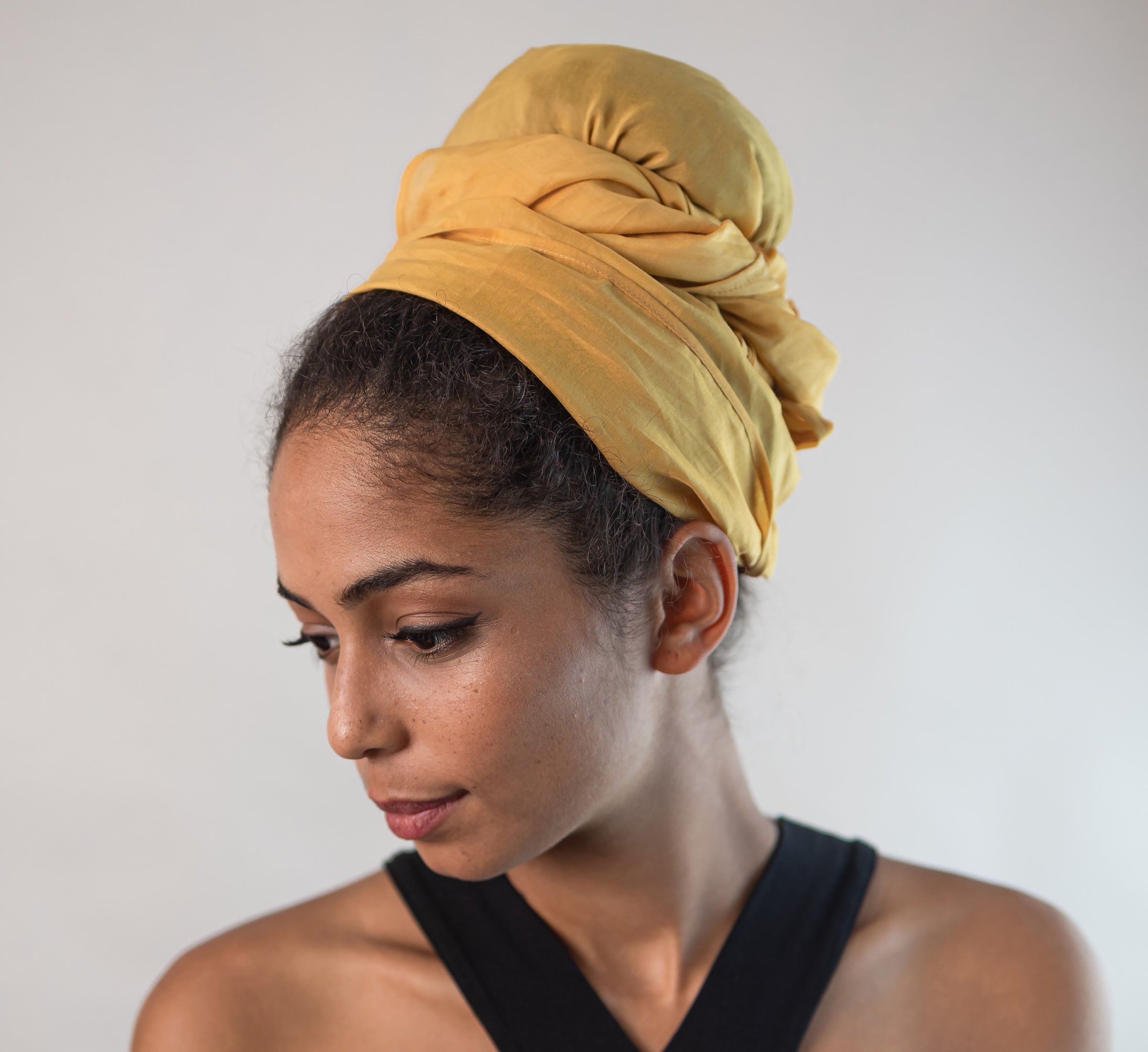 Eine junge hübsche Frau mit naturkrausen Haaren trägt ein Kopftuch aus gelber Baumwollseide und schaut verträumt zur Seite