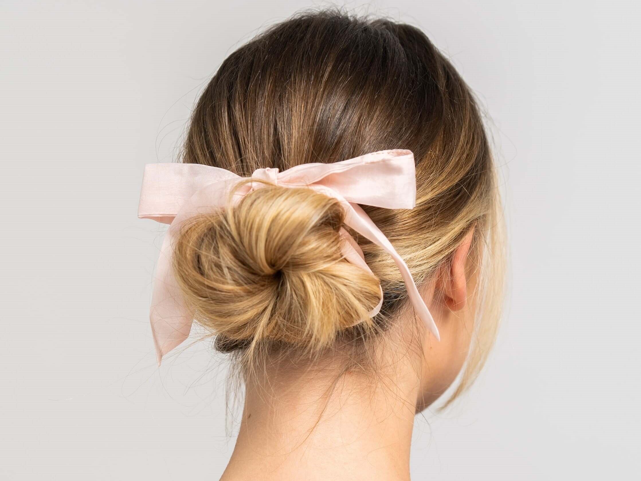 Schöne Frau mit blonden Haaren trägt ein rosa farbenes Haarband von Curly'N'Covered als Schleife im Haar