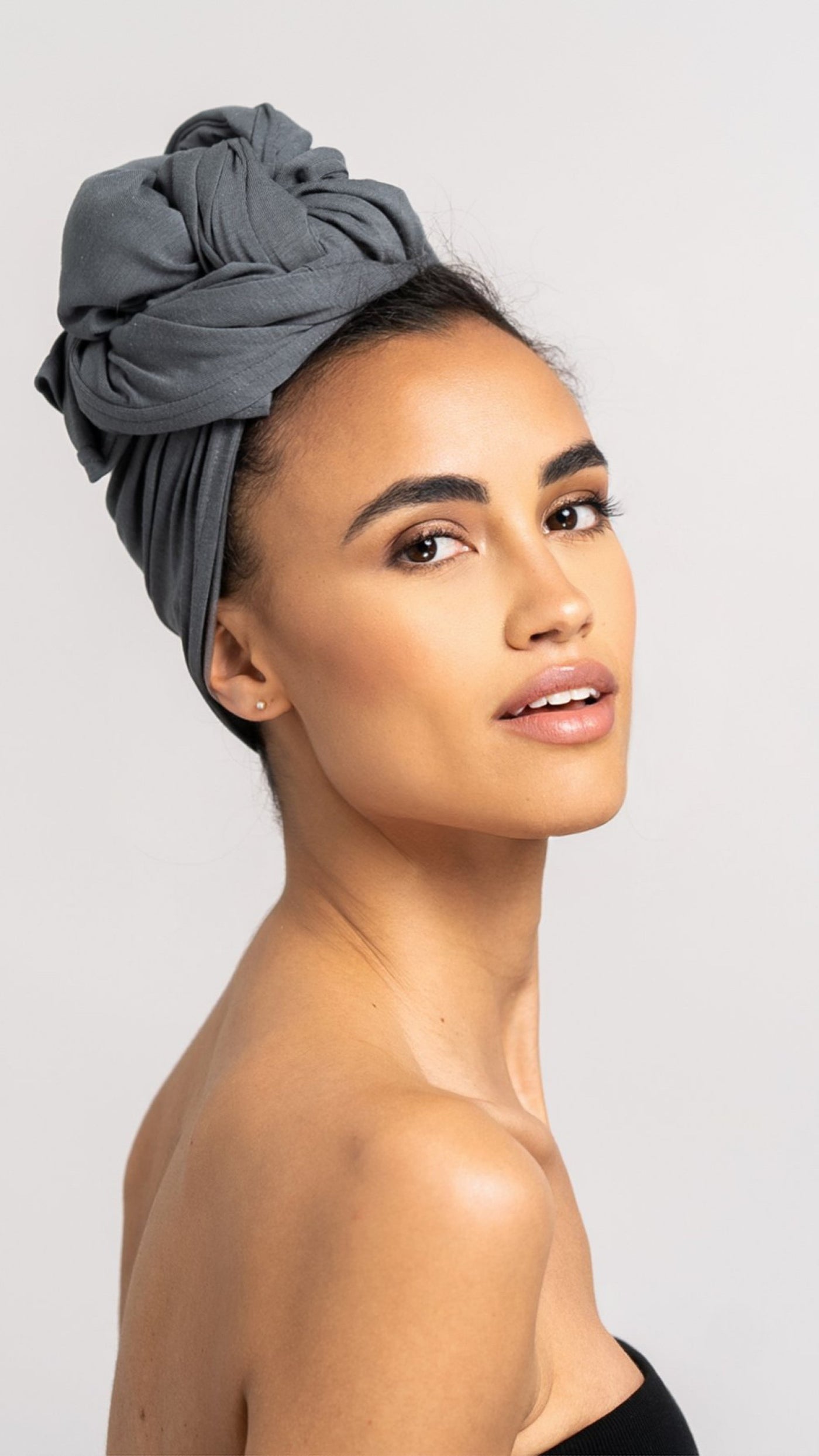 Seitenansicht von einer hübschen Frau, die ein graues Bambus Haar Handtuch von Curly'N'Covered als Turban trägt und dabei ihren Kopf in Richtung Kamera dreht