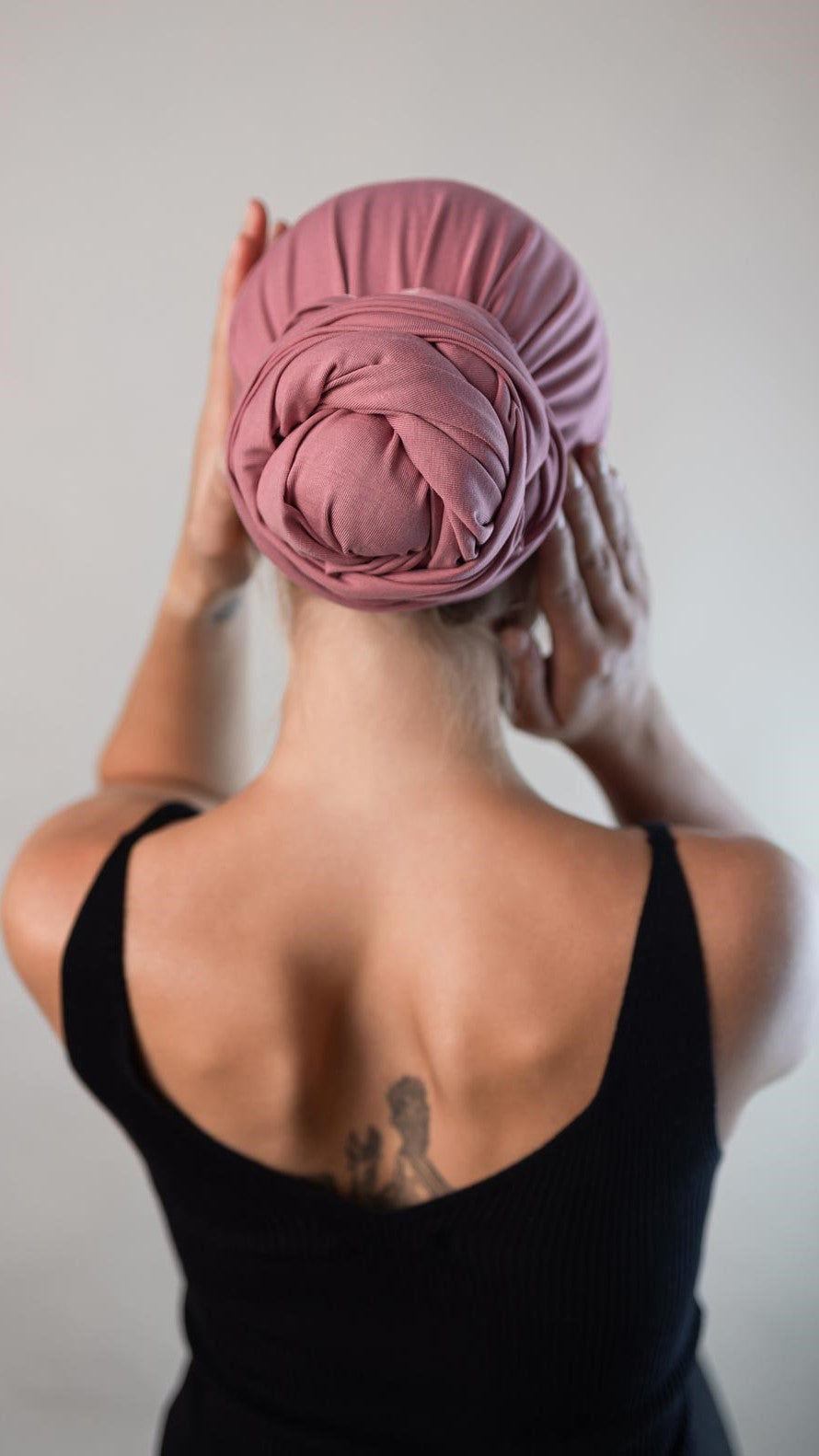 Rückansicht von einer hübschen Frau, die ein rosa Bambus Haar Handtuch von Curly'N'Covered als Turban trägt und dabei ihre Hände um den Turban legt