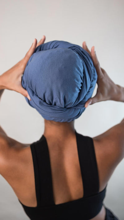 Rückansicht von einer hübschen Frau, die ein hellblaues Bambus Haar Handtuch von Curly'N'Covered als Turban trägt und dabei ihre Hände um den Turban legt