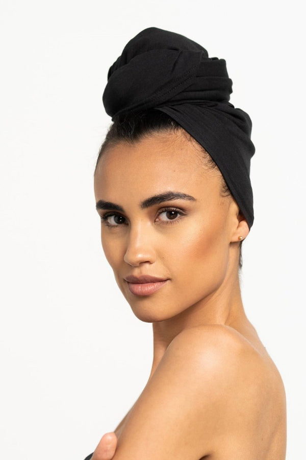 Schöne Frau mit dunklen Locken trägt ein Bambus Haar Handtuch in Schwarz mit den Maßen 55 x 120 von Curly N Covered als Turban gewickelt
