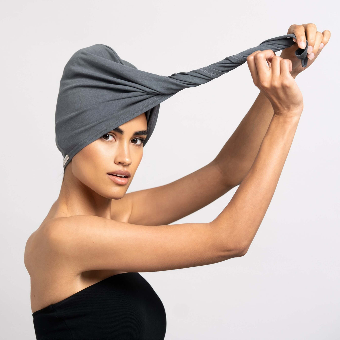 Bildschöne Frau zwirbelt Bambus Turban Handtuch von CURLY N COVERED zu einem Turban um die Haare sanft anzutrocknen