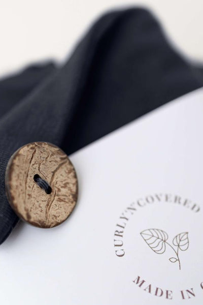 Detailaufnahme des Kokosnussknopfs und der Banderole des Bambus Turban Handtuchs in schwarz von CURLY N COVERED