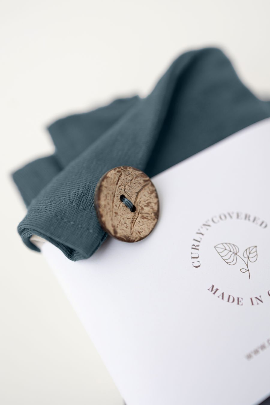 Makroaufnahme des Kokosnussknopfs und der Banderole des Bambus Turban Handtuchs in stahlblau von CURLY N COVERED