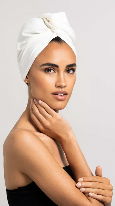 Bildschöne Frau im Seitenprofil dreht Kopf Richtung Kamera und trägt weißes Bambus Turban Handtuch von Curly'N'Covered als Turban gewickelt