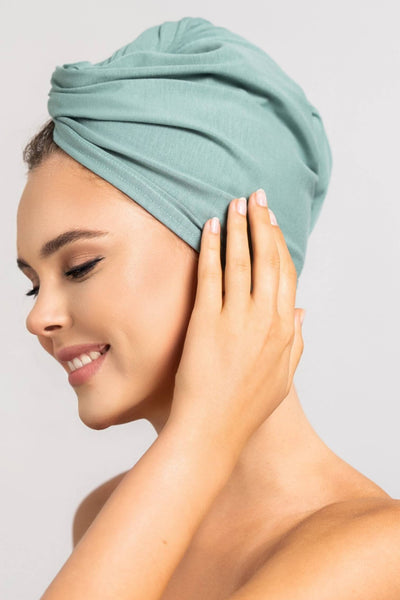 Bildschöne Frau trägt mint grünes Bambus Turban Handtuch von Curly'N'Covered als Turban gewickelt und streicht sich mit der Hand über den Turban