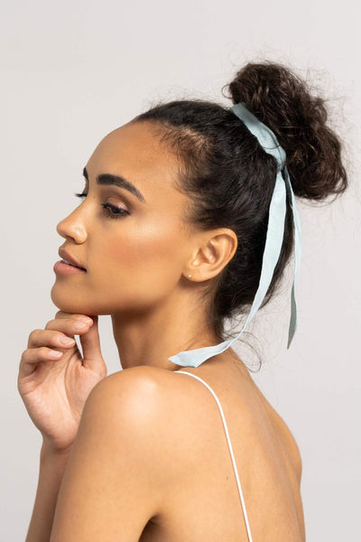 Wunderschöne Frau mit dunklen Locken trägt ein hellblaues Haarband aus Baumwollseide von CURLY N COVERED um ihren Dutt