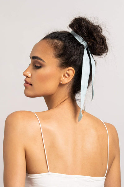 Wunderschöne Frau mit dunklen Locken trägt ein Haarband in hellblau aus Baumwollseide von CURLY N COVERED um ihren Dutt