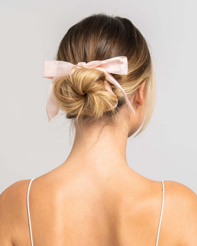 Wunderschöne Frau mit blonden Haaren trägt Haarband aus Baumwollseide in rosa von Curly'N'Covered als Schleife im Haar