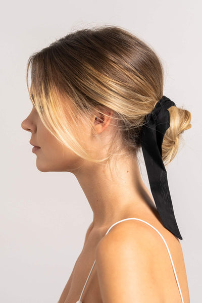 Wunderschöne Frau mit blonden Haaren trägt ein schwarzes Haarband aus Baumwollseide von CURLY N COVERED um ihren Dutt