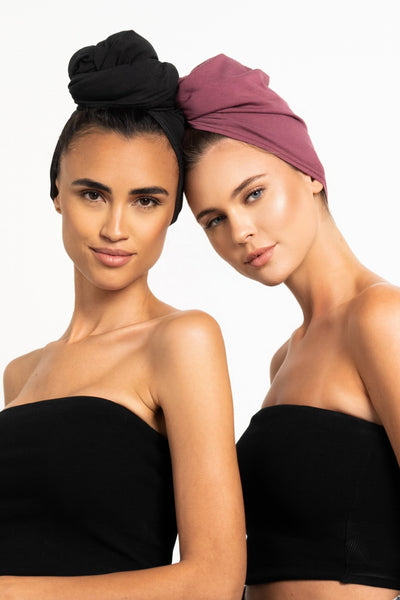 Zwei schöne Frauen tragen Locken Handtücher aus Bambus von CURLY N COVERED als Turbane gewickelt, ein Tuch ist in schwarz, das andere in rot