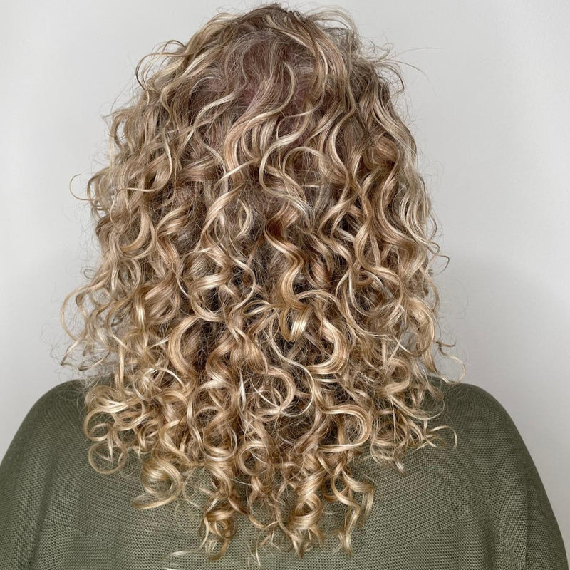 Hinterkopf einer blonden Frau mit Locken, die durch das Verwenden einen Schlafhaube aus Seide gesund und voller Vitalität und Sprungkraft sind.