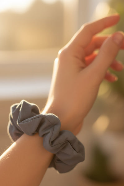 Ein grauer Scrunchie aus Bambus-Stoff von Curly N Covered als Accessoire am Handgelenk