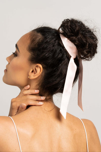 Wunderschöne Frau mit dunklen Locken hat einen rosa farbenen Seidenschal von Curly N Covered als Haarband um ihre Haare gebunden.