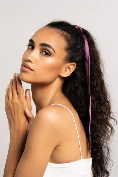 Wunderschöne Frau mit langen dunklen Locken hat einen Seidenschal für Damen in Pflaume von Curly N Covered in ihre Haare geflochten.