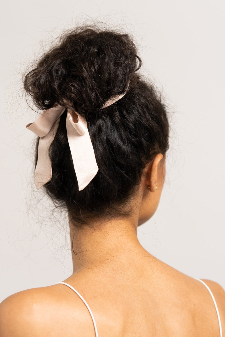 Bildschöne Frau mit dunklen Locken trägt ein sandfarbenes Haarband aus 100% Maulbeerseide von CURLY N COVERED um ihren Dutt