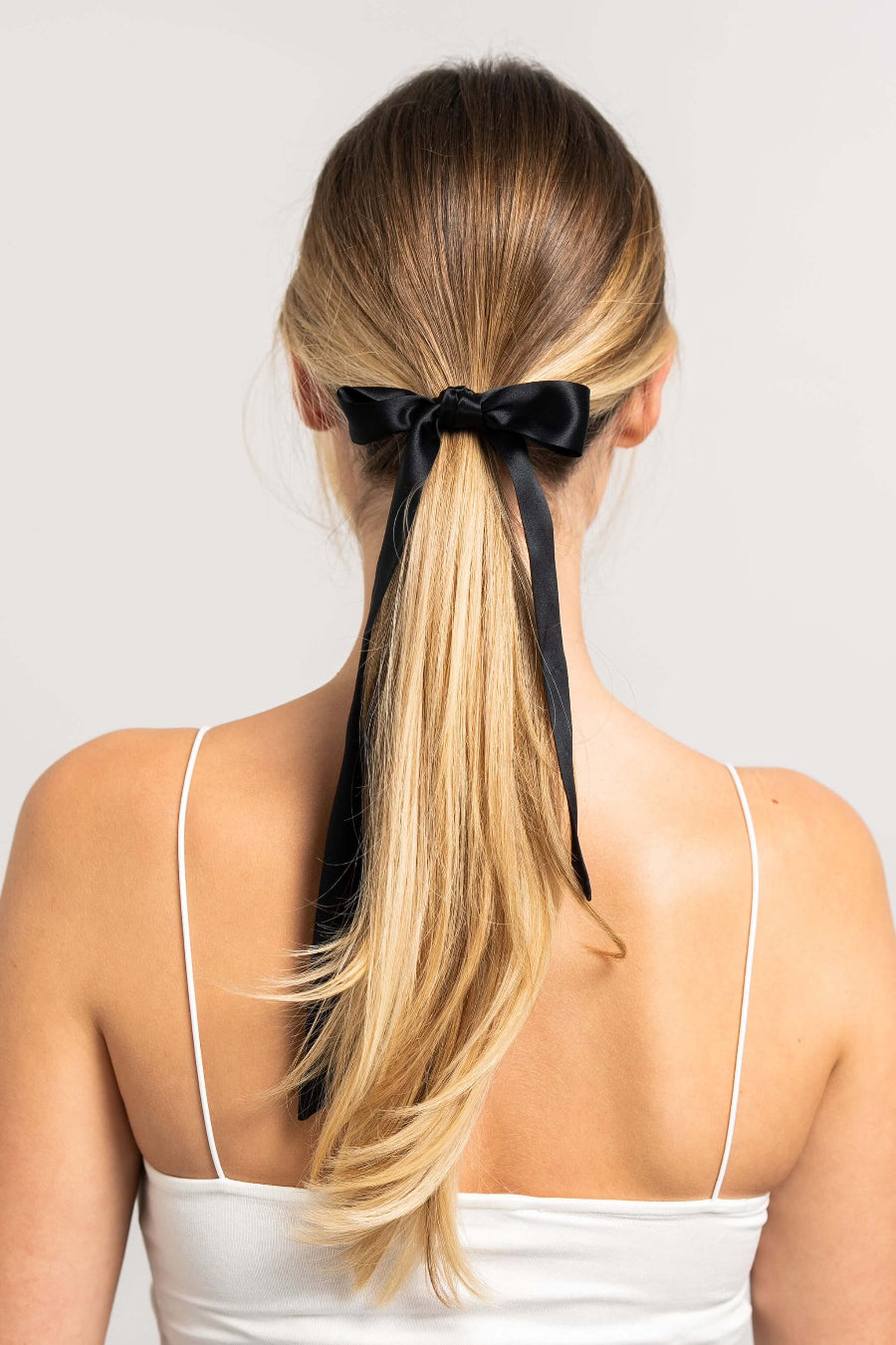 Wunderschöne Frau mit langem blonden Pferdeschwanz hat einen schwarzen Seidenschal für Damen von Curly N Covered als Schleife um ihren Zopf gebunden.