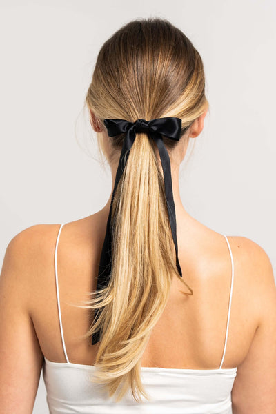 Wunderschöne Frau mit langem blonden Pferdeschwanz hat einen schwarzen Seidenschal für Damen von Curly N Covered als Schleife um ihren Zopf gebunden.