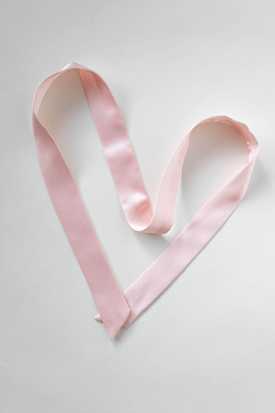 Seidenschal aus reiner Maulbeerseide in rosa von Curly N Covered vor weißem Hintergrund als Herz ausgelegt