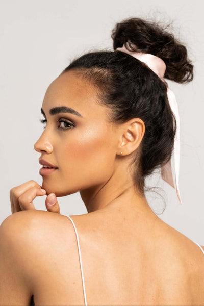 Wunderschöne Frau mit dunklen Locken hat einen rosa farbenen Seidenschal von Curly N Covered als Haarband um ihre Haare gebunden und schaut zur Seite, während sie sich mit der Hand ans Kinn fasst.