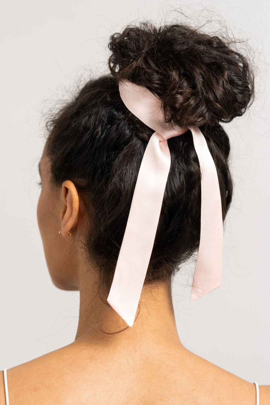 Wunderschöne Frau mit dunklen Locken hat einen rosa farbenen Seidenschal von Curly N Covered als Haarband mit Schleife um ihre Haare gebunden.