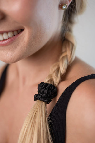 Geflochtener Zopf mit langen blonden Haaren, zusammengehalten durch einen Mini Scrunchie aus reiner Maulbeerseide in der Farbe Schwarz von CURLY N COVERED